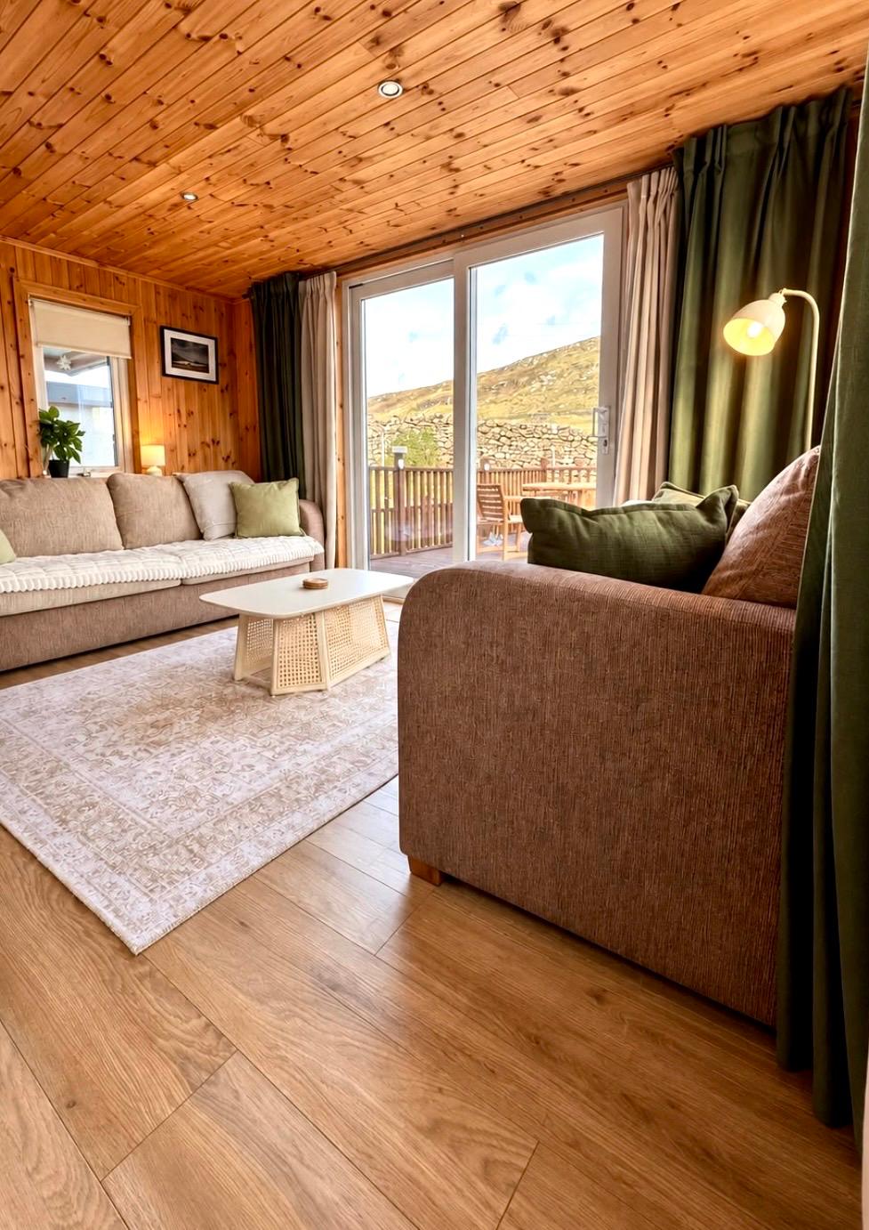 Timber-lined living room with sofas and glass doors opening onto the decking